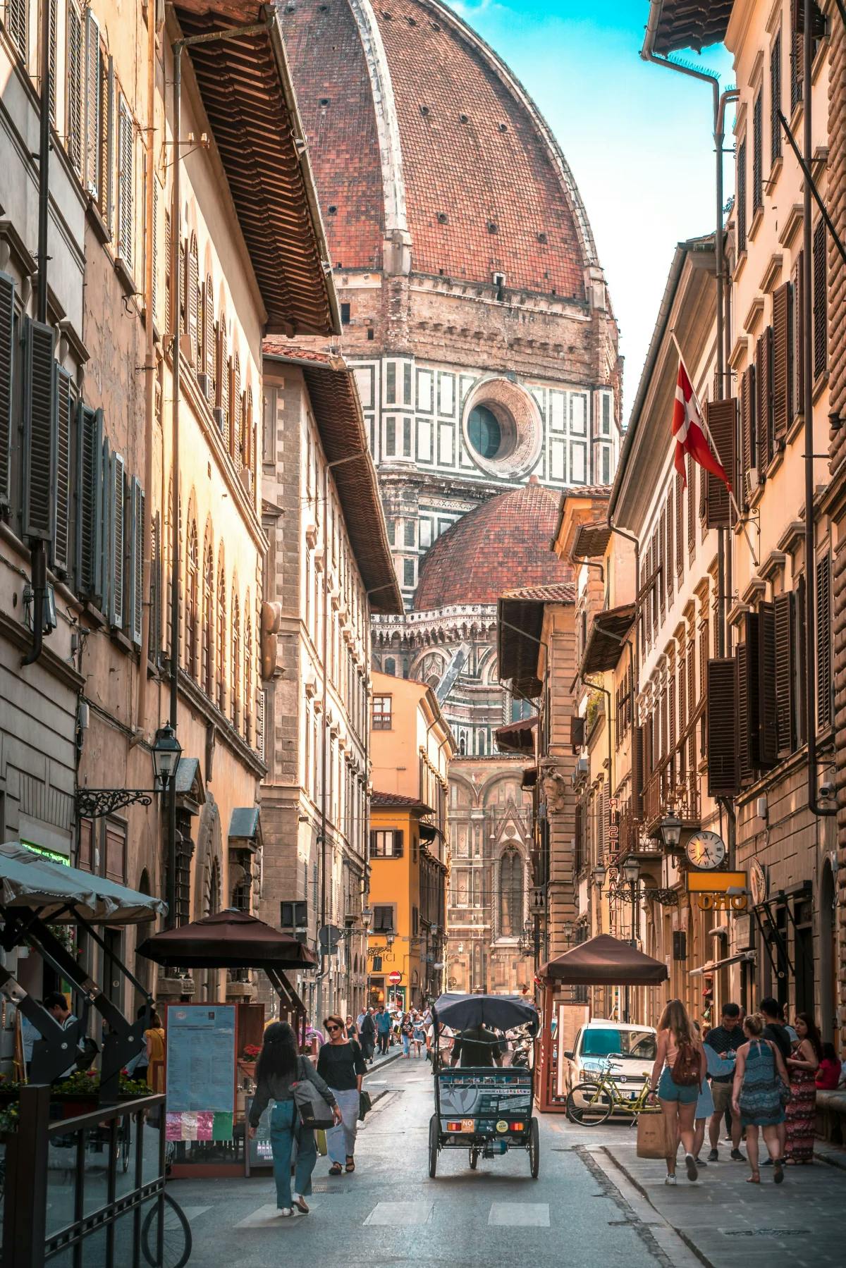 A contrasting look at Florence's grandiose Duomo through the narrow point of view of residential buildings, pedestrians and street carts.