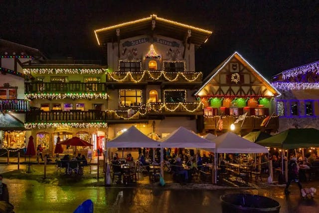 The exterior of a Bavarian-style, winter village, with lights, tables, tents and Christmas decorations.