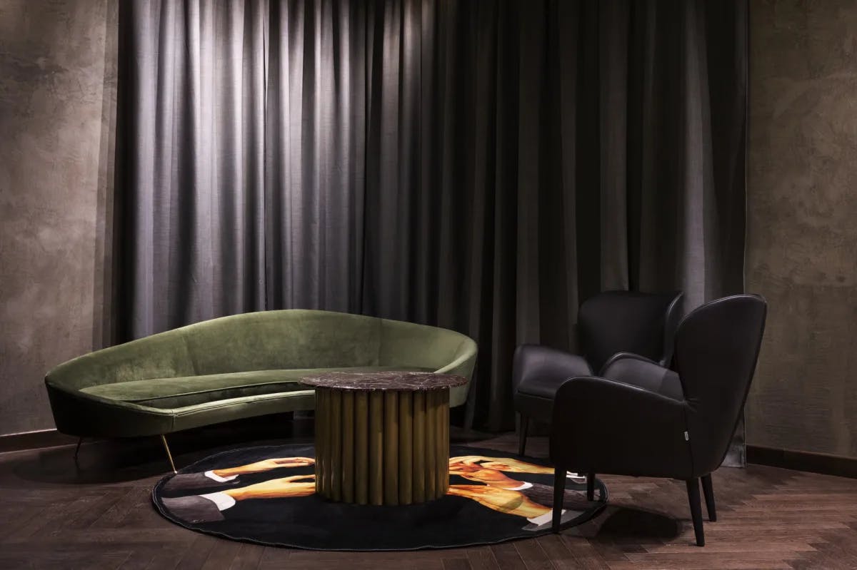 a green velvet couch and a black chair in a dimly lit lounge