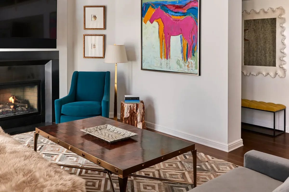 a cozy living room with a blue velvet chair and a colorful painting hanging on a white wall