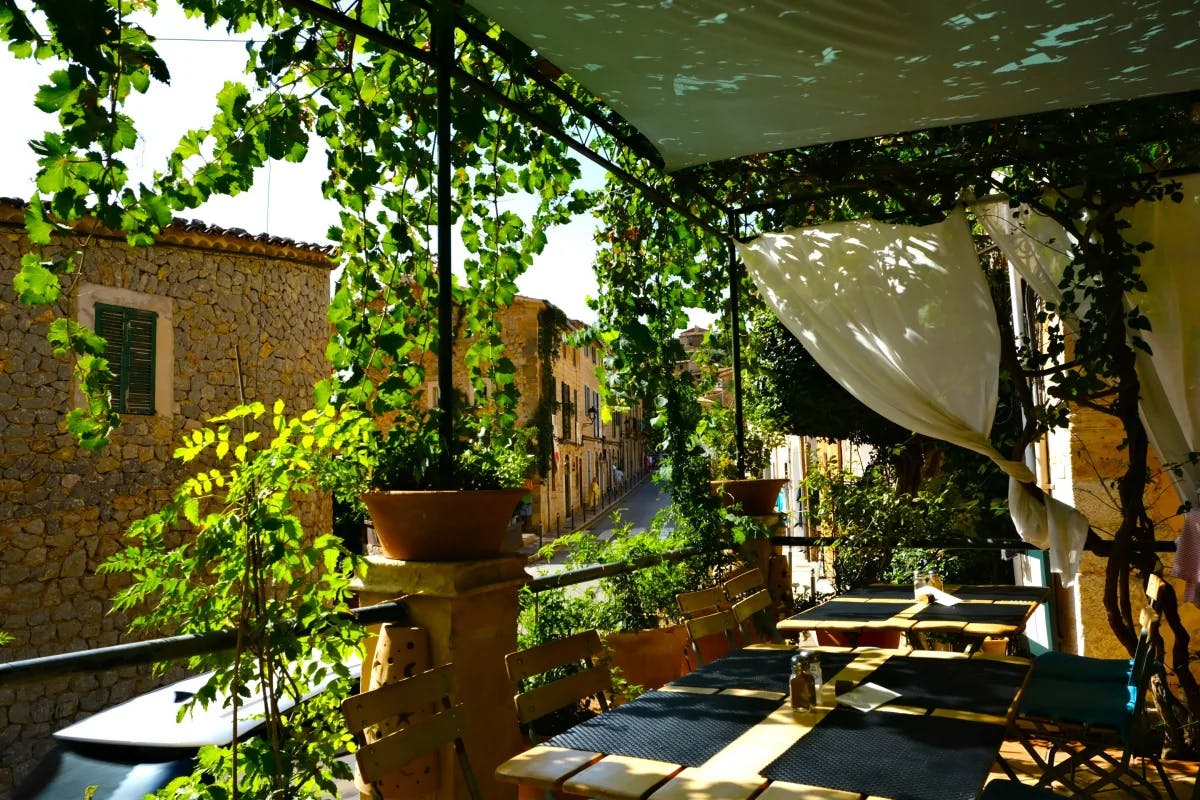 A picture of a patio with tables, chairs and greenery during daytime.