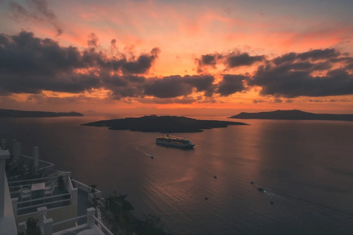 An orange sun is setting over the ocean with islands in the distance.