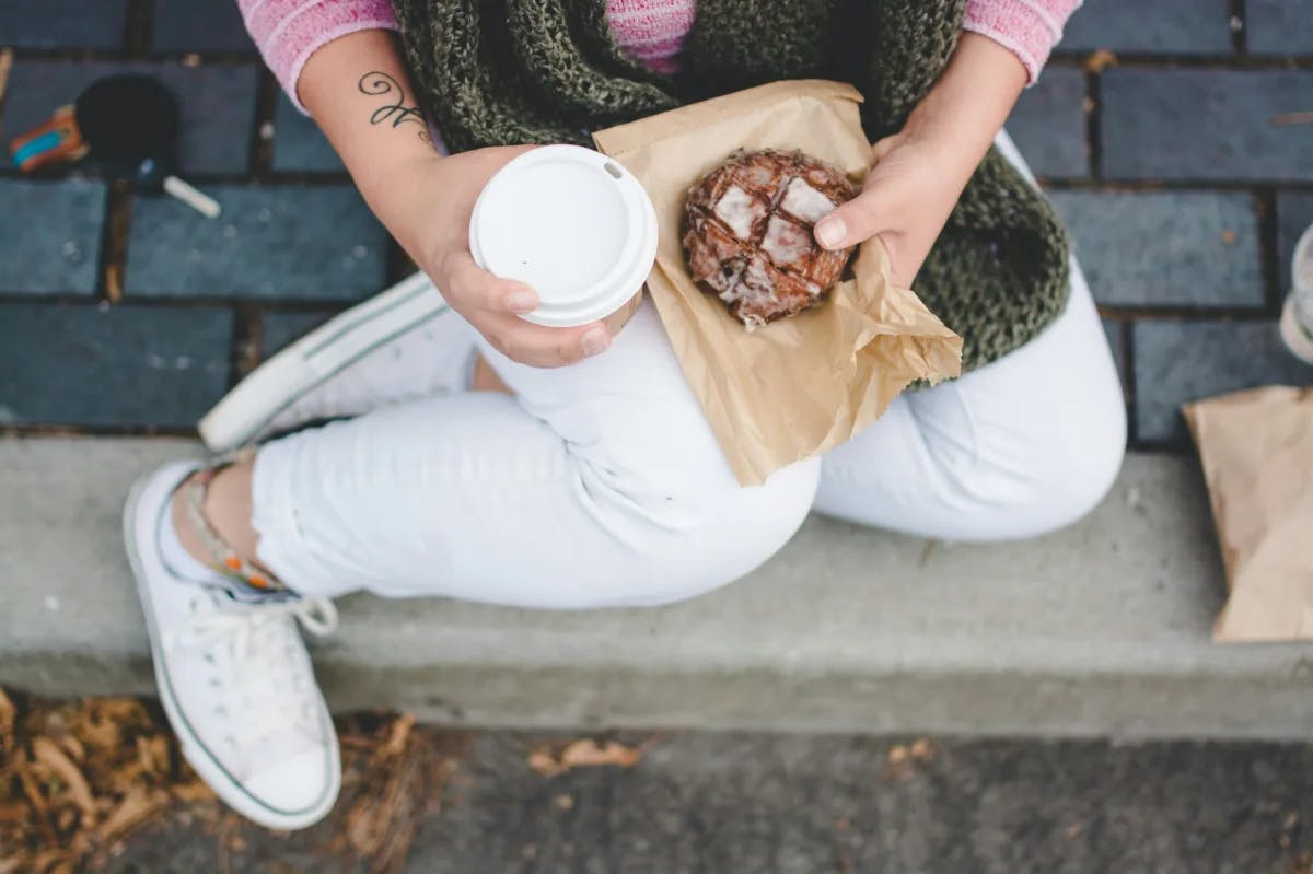 A person holding coffee and pastry.