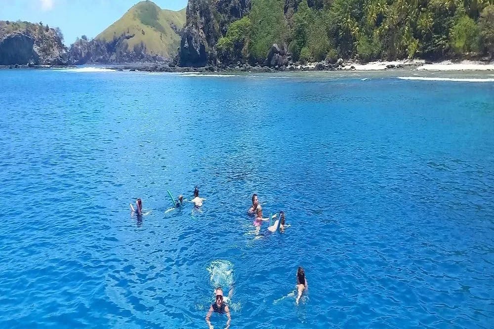 A picture of people Swimming in the Mamamuca Islands during the daytime over blue water with green mountains in the background. 