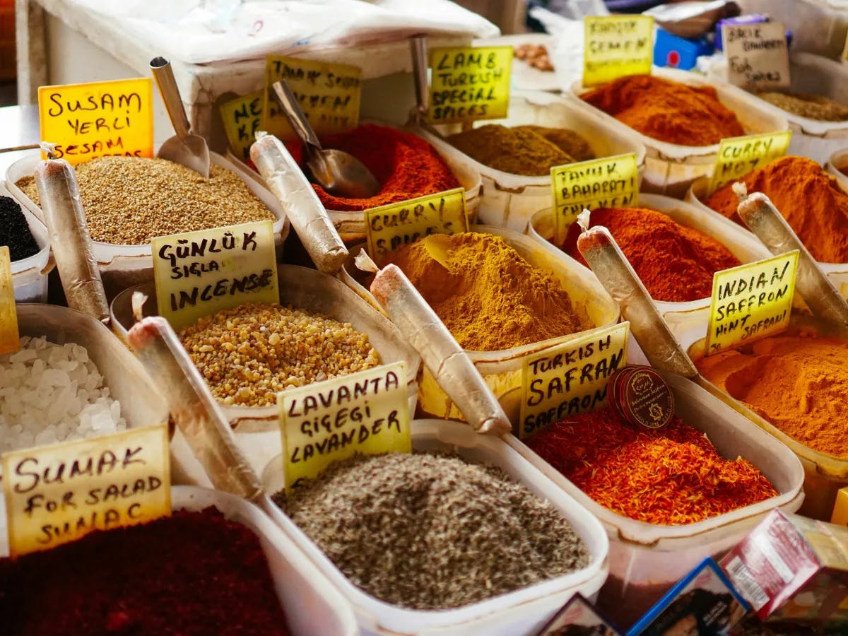 A colorful array of spices and grains, each labeled in Turkish, in open bags.