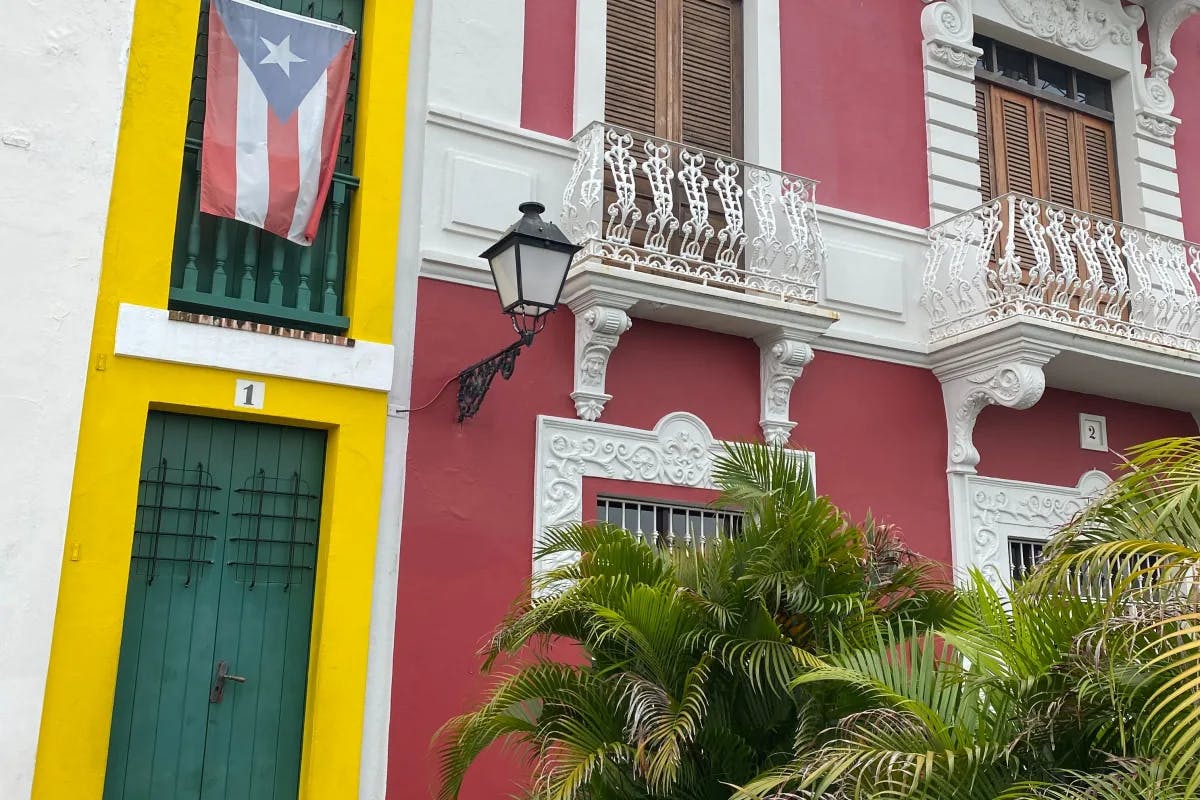 A colonial style building painted red and yellow with a Puerto Rican flag flying on a railing