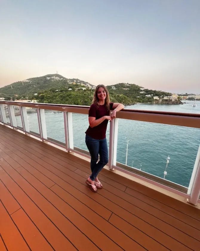 Advisor posing on the edge of a balcony with the ocean in the distance on a sunny day. 