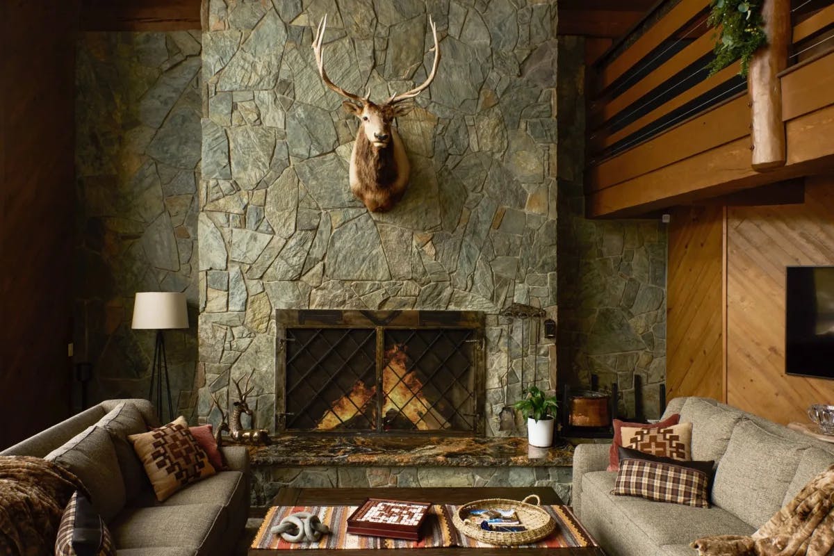 huge stone fireplace with a deer head mounted above it and two couches facing each other with a table in between