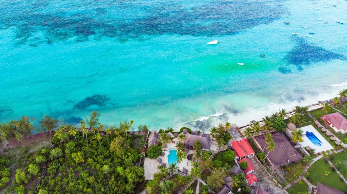 An aerial view of a coastline with local houses, lush greenery, and crystal-clear, turquoise waters.