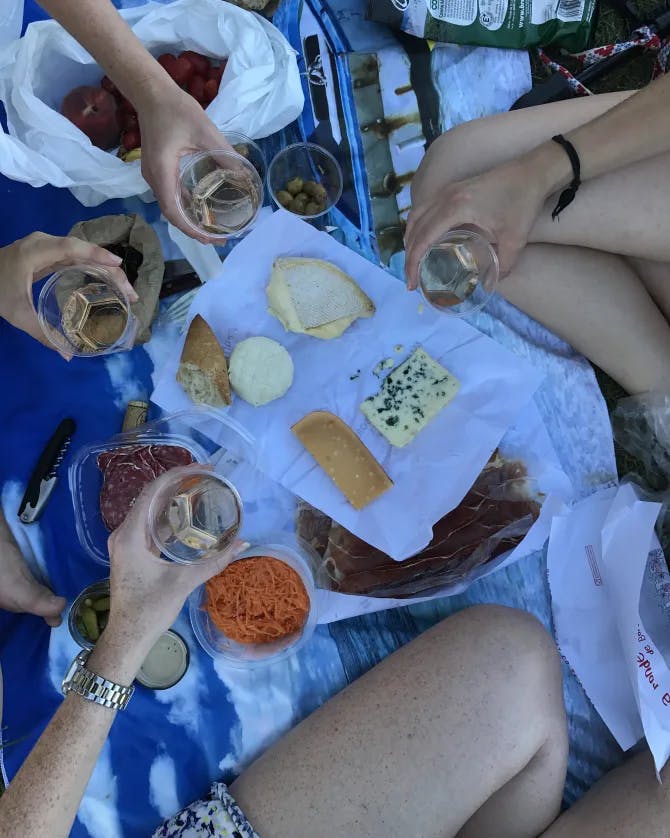 A birds eye view of a picnic setting between three people with wine and cheeses