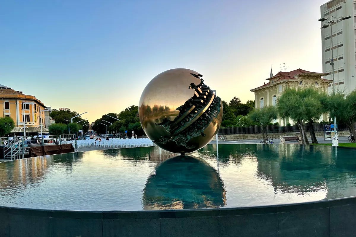 A massive silver globe sculpture positioned in the middle of a fountain.