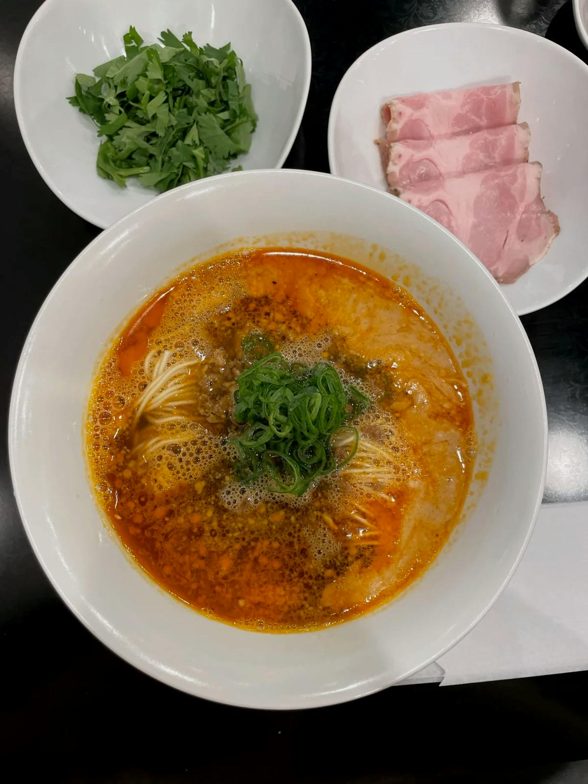 An aerial view of a traditional Japanese broth served in a white bowl and side dishes of sliced cold meat and greens