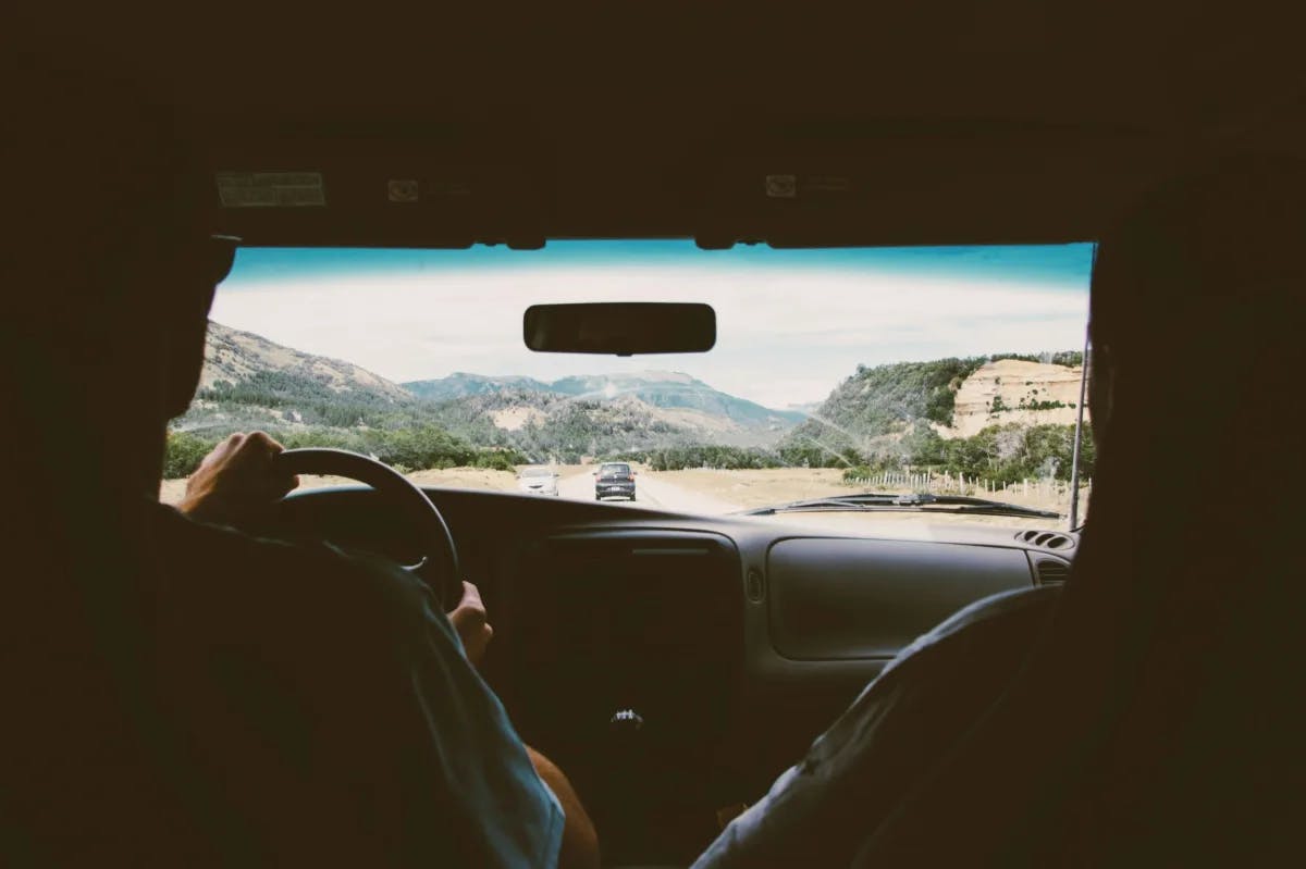 person driving a car looking out onto the road with mountains beyond