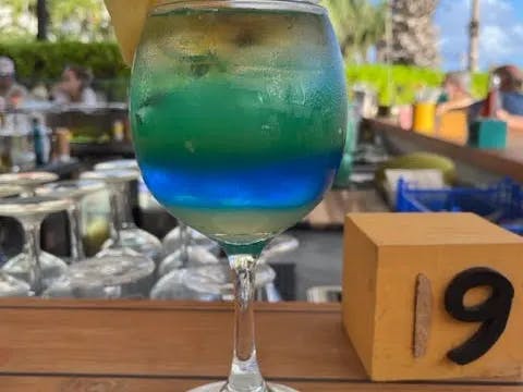 A close-up image of a green and blue beverage placed on top of a bar. 