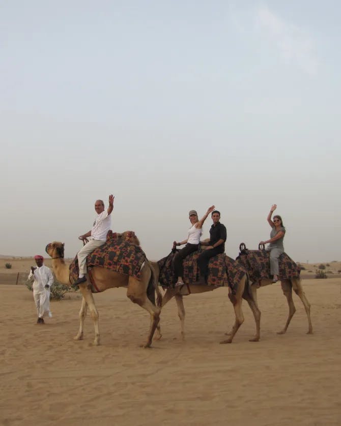 A photo of three people on a camels on a sand dune.