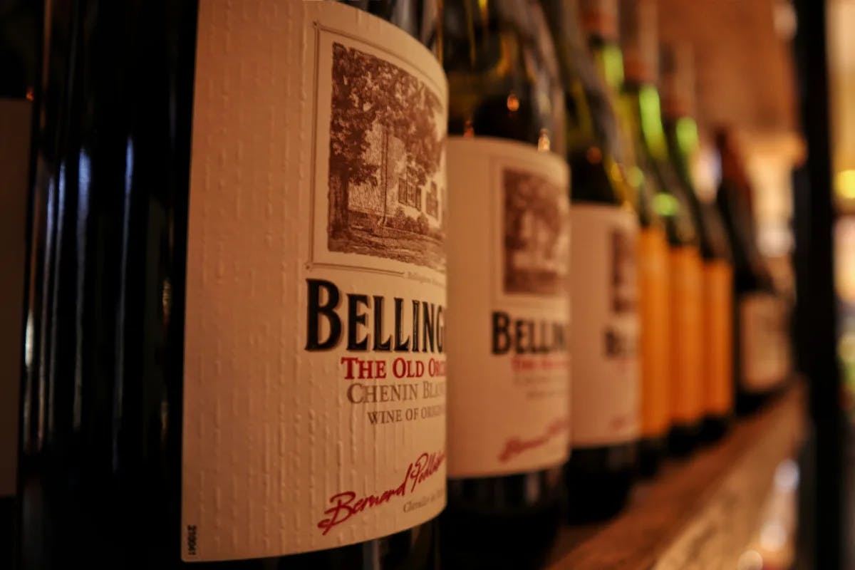 A row of classy wine bottles lined up on a restaurant's shelf, illuminated by intimate lighting. 