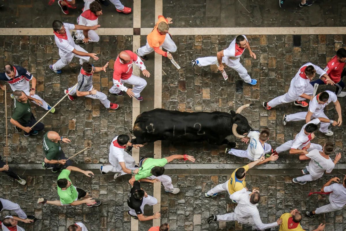 A bull running down a brick road with people in white and red outfits running alongside it. 