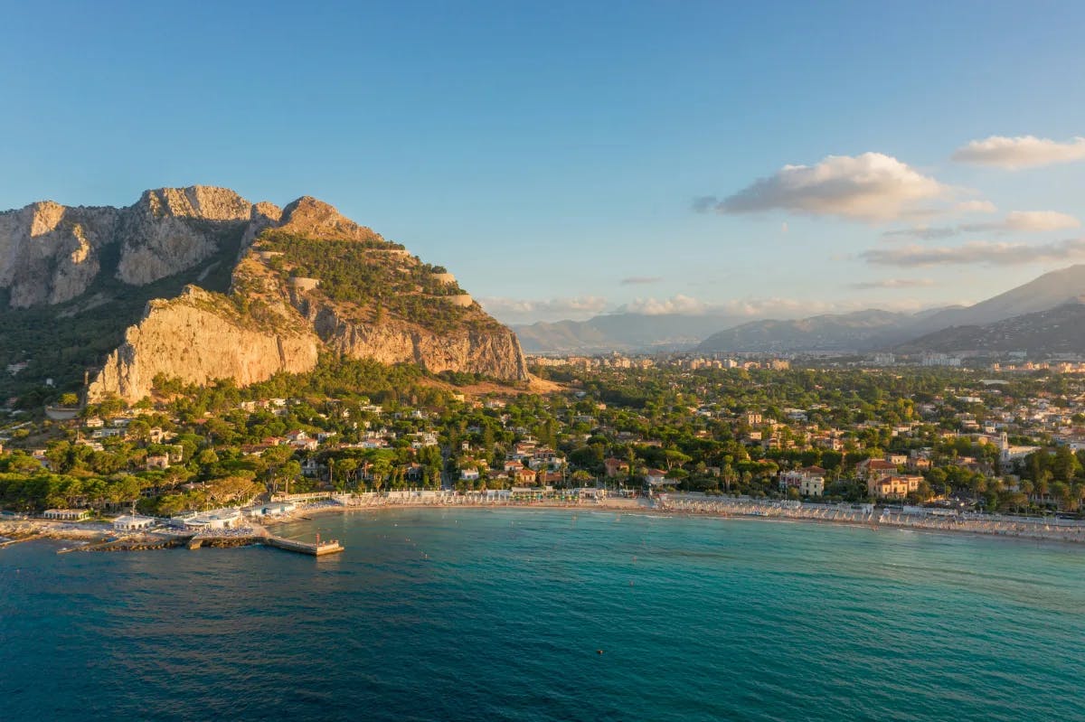 A beautiful view of the coastline of Palermo with hills and buildings scattered amid lush greenery.