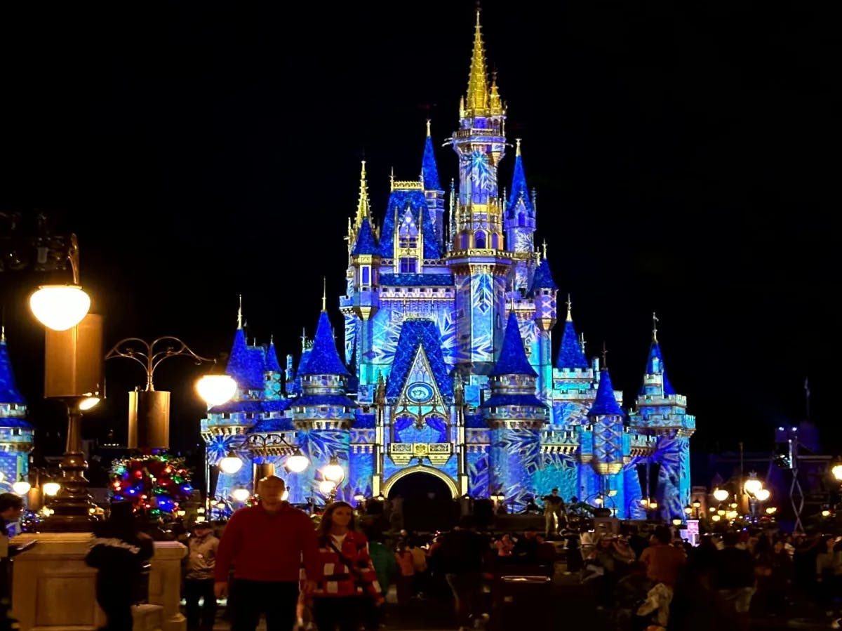 A picture of people standing in front of a blue lit-up Disney castle at nighttime.