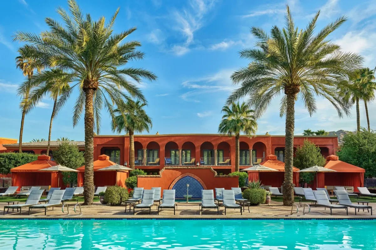 a pool in front of a red-adobe building flanked by palm trees