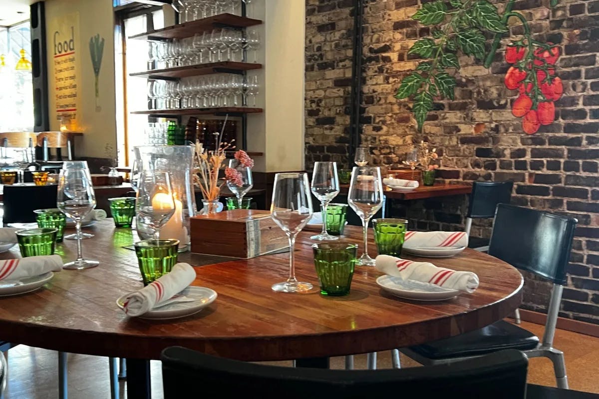 table setting with green glasses and an exposed brick wall with a plant mural in the background