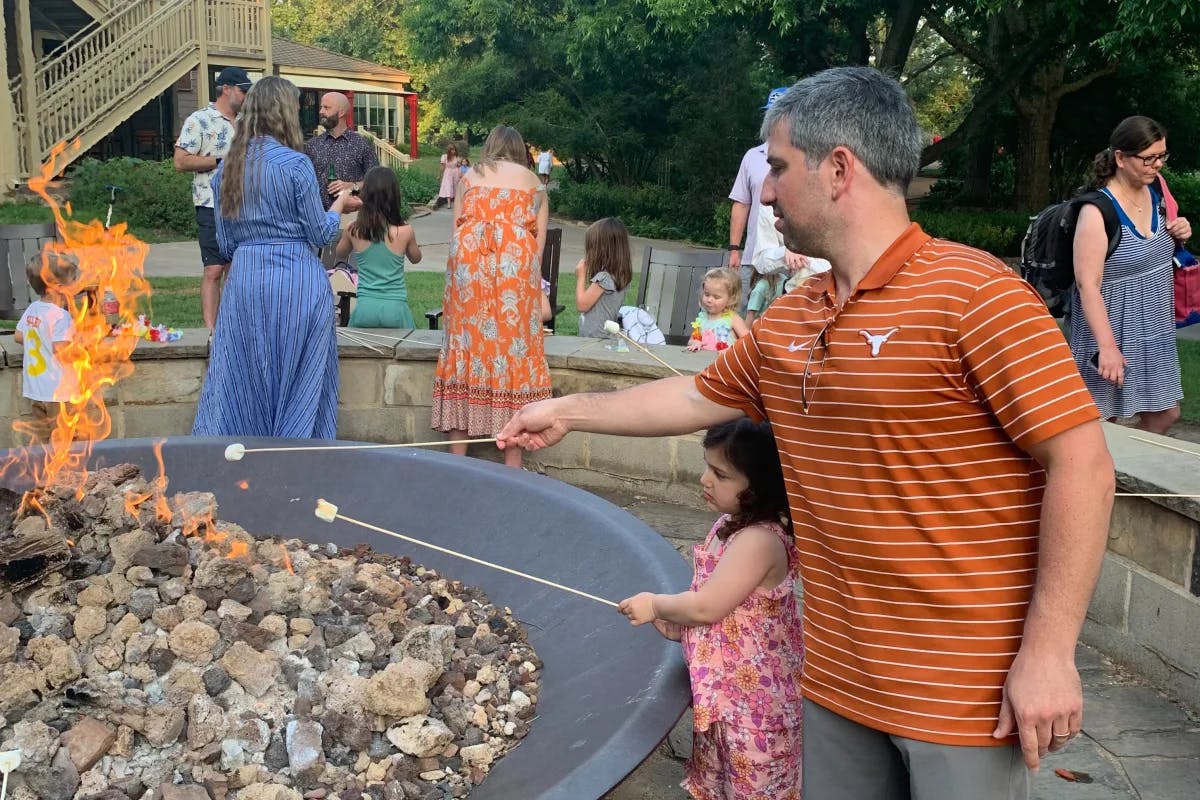 A group of people roasting marshmallows in a fire pit outside