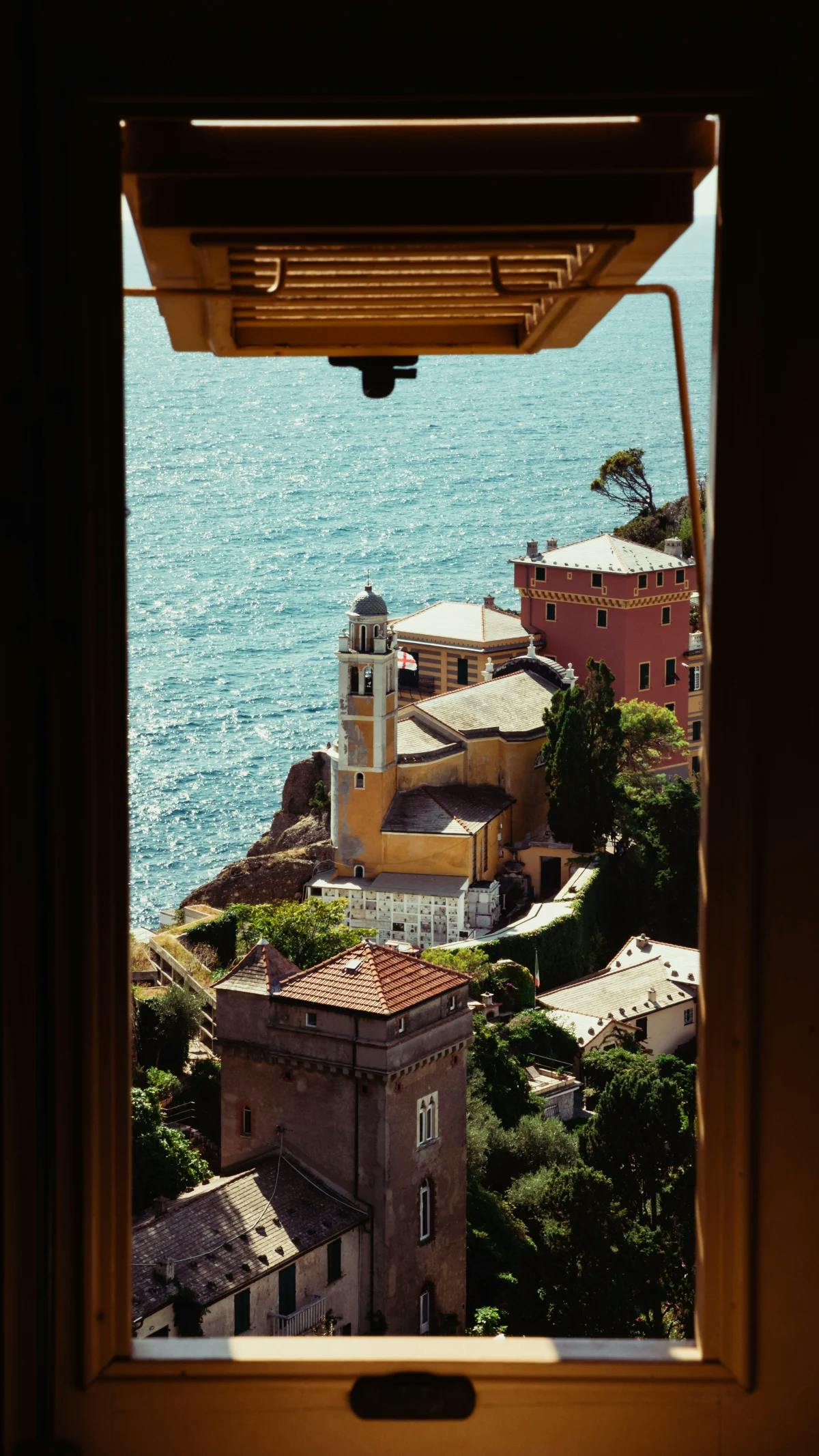 Looking through a window frames a view of Genoa's coast, with residential buildings and the big, blue sea.