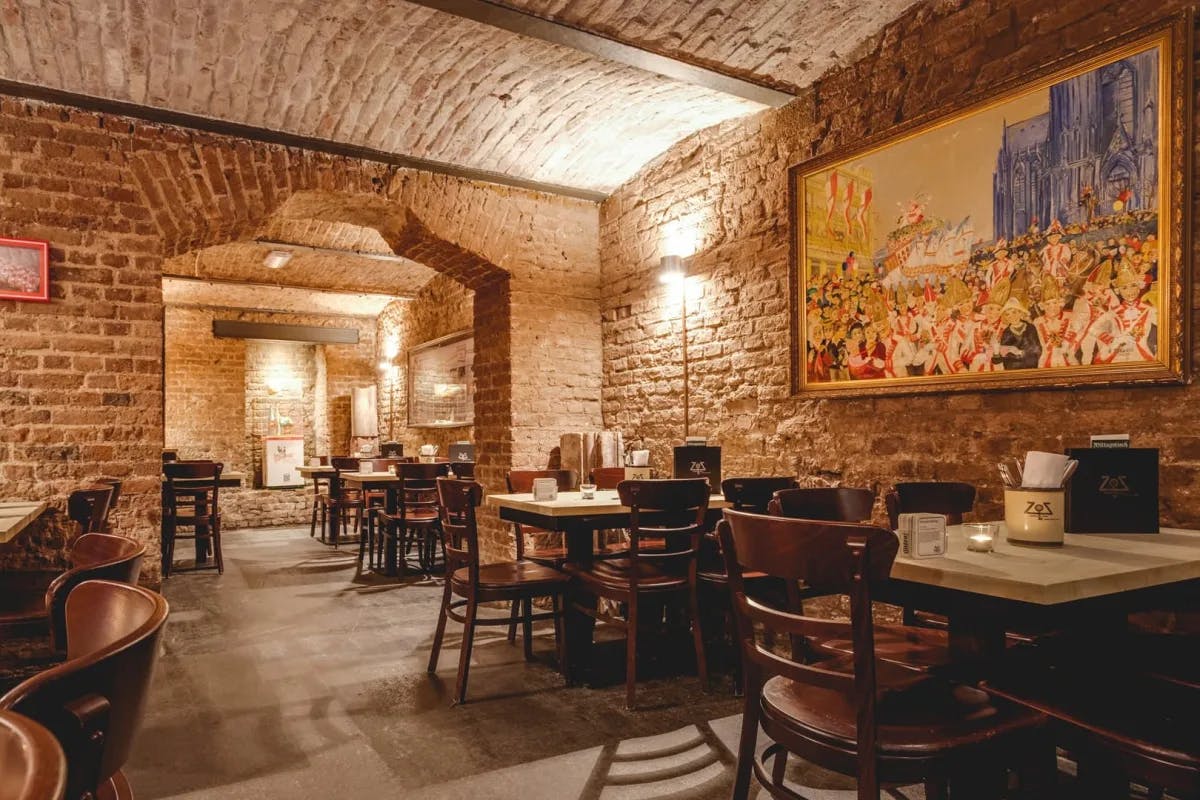 An underground brick restaurant with tables and a colorful painting on the wall.