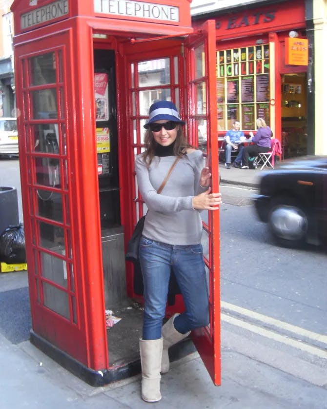 Maggie in a grey shirt in a red phonebooth.
