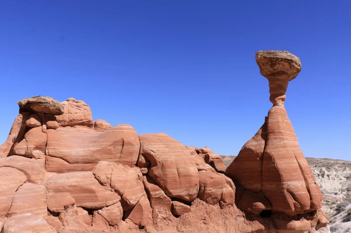 Red rock formations, one pyramid shaped with a large rock balanced at the very top in the desert.