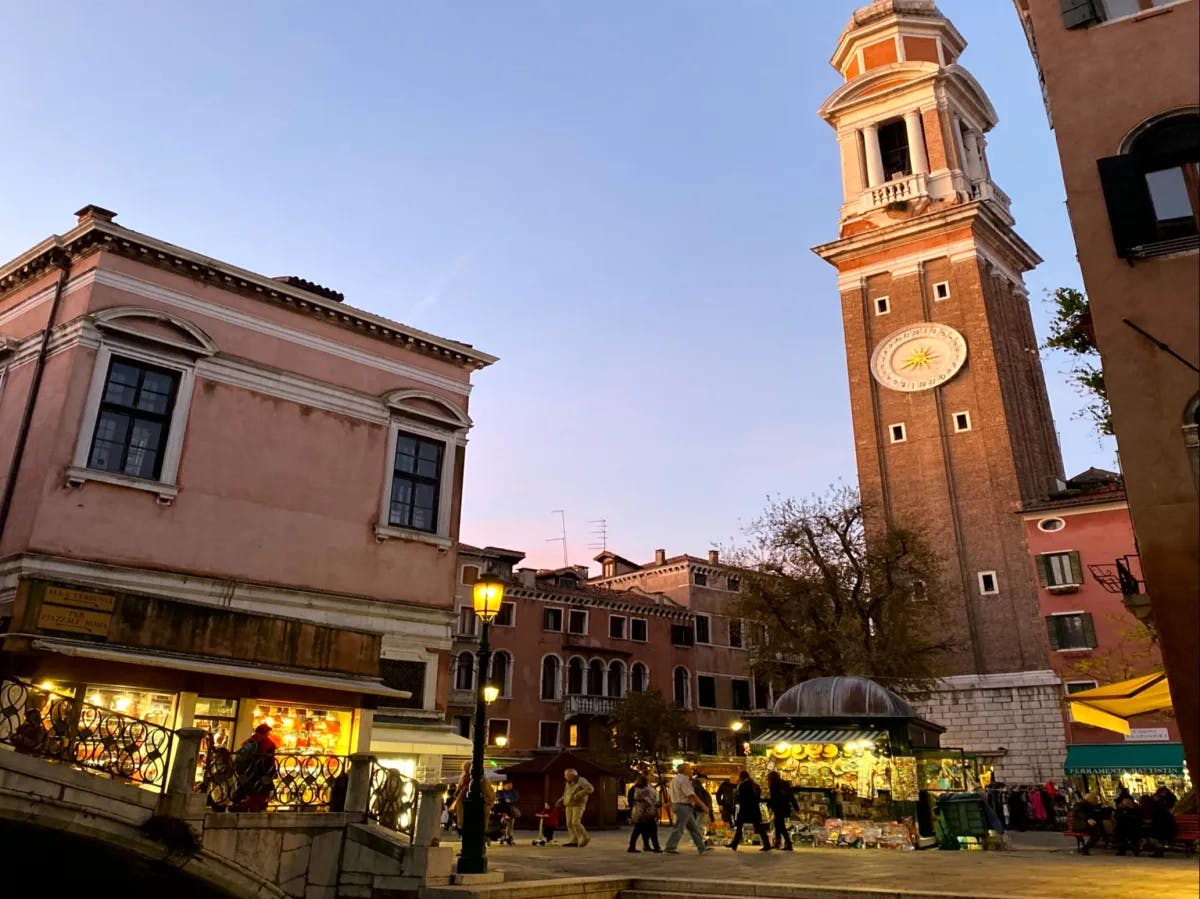 A twilight view of a European-style building with a clock tower, illuminated against the evening sky.