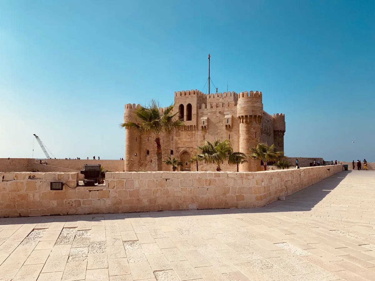 A stone temple in the desert with palm trees on a clear day