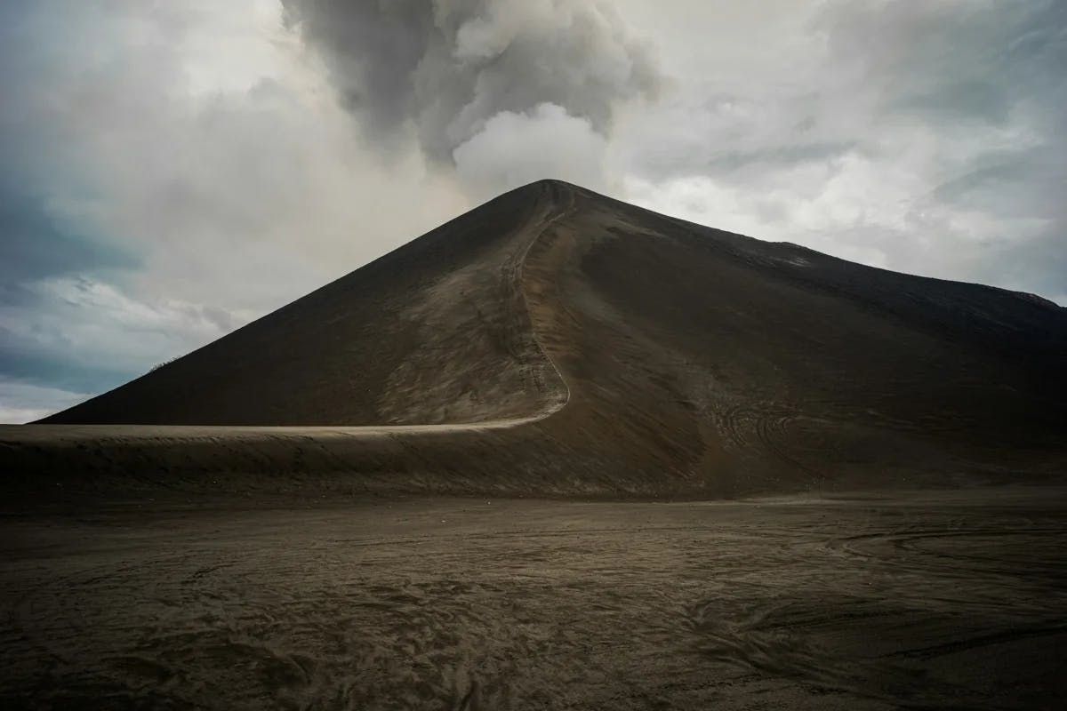 A view of a path leading to the top of Mount Yasur with smoke billowing from the top of the volcano.