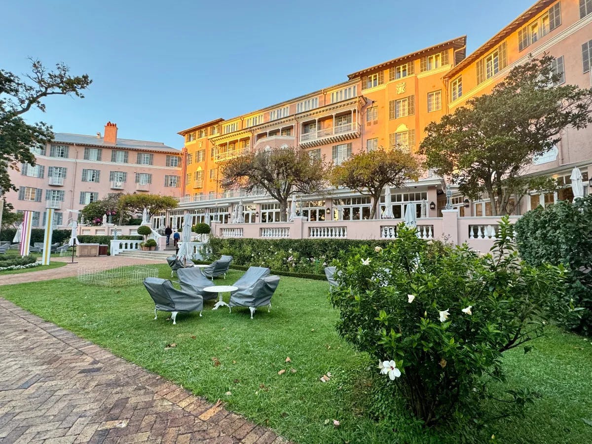 The Belmond hote, a grand pink building with white balconies, set amidst lush greenery under a clear dusk sky.