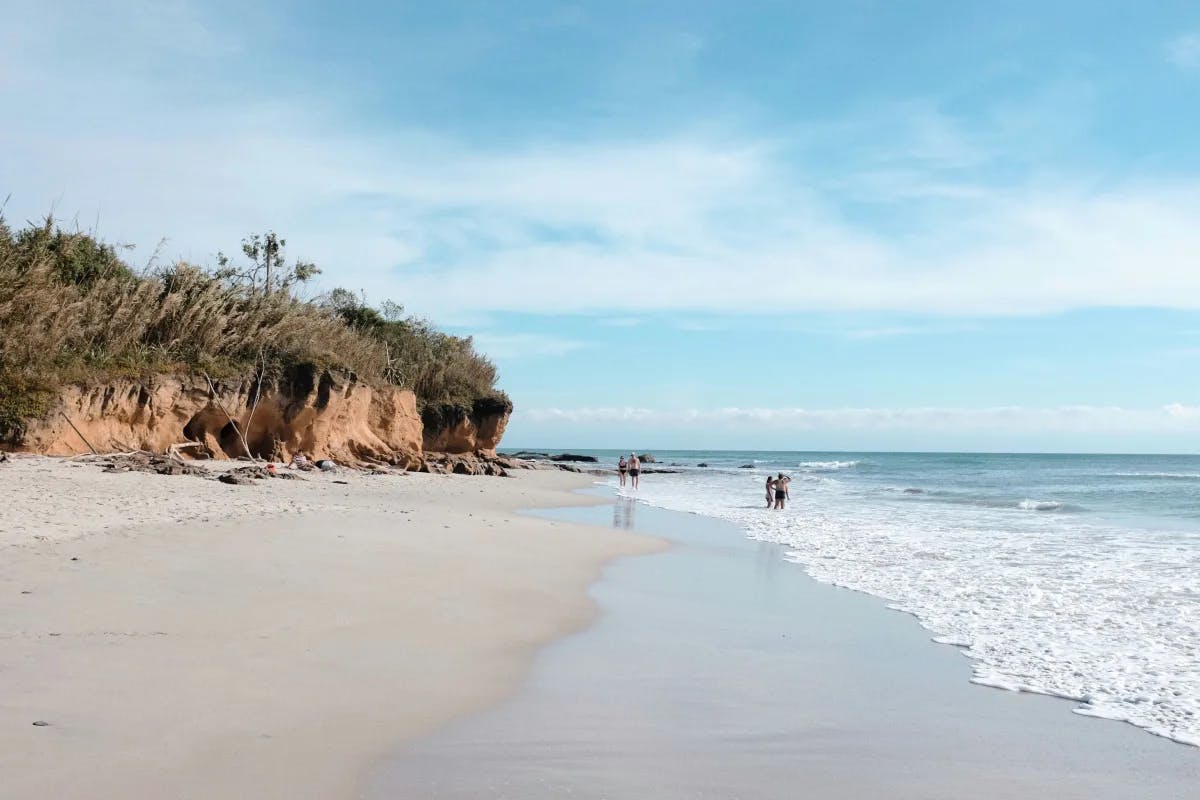 A view of the coastline of a beach in Punta Minta, with people in the distance standing in the water.