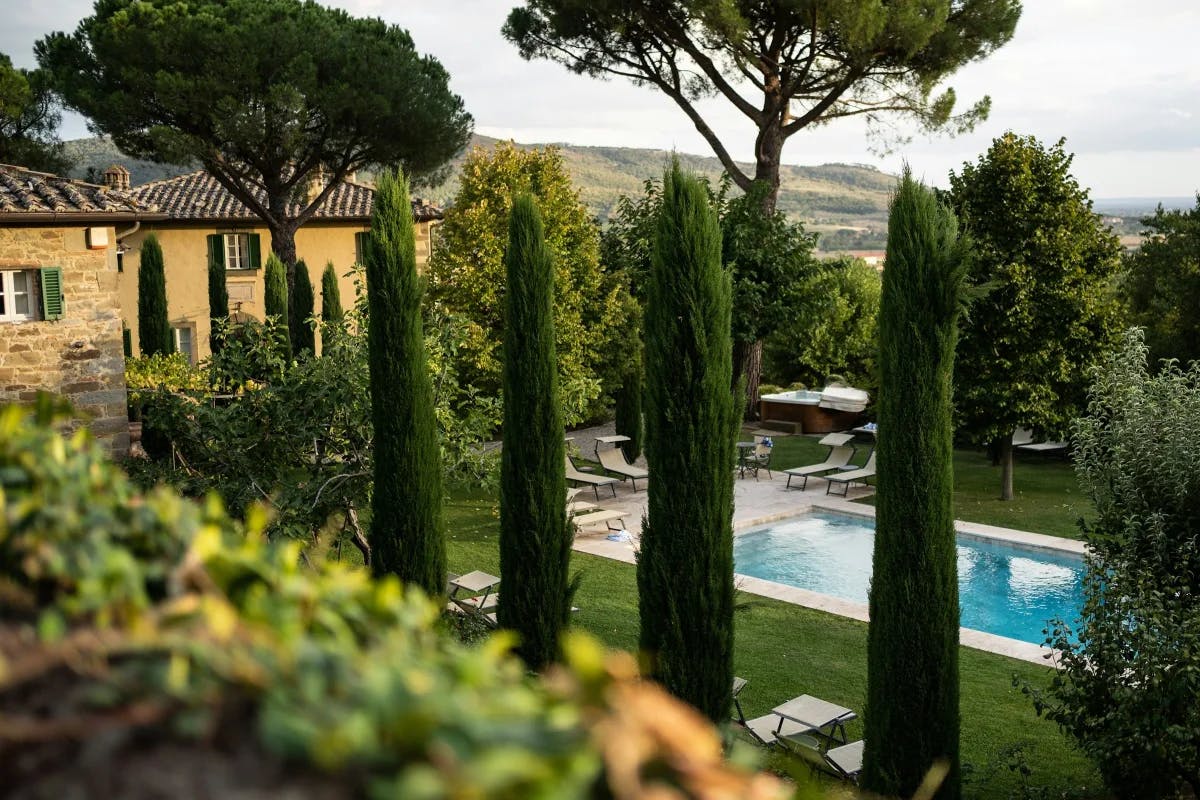 A view of a stone and yellow Italian villas, trees and a swimming pool surrounded by a beautiful green lawn. 