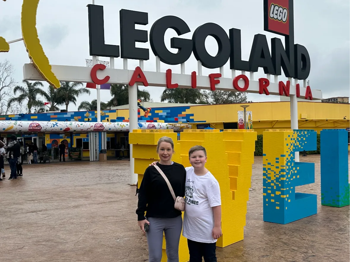 A picture of a woman standing with a child in front of a place called Legoland during daytime.