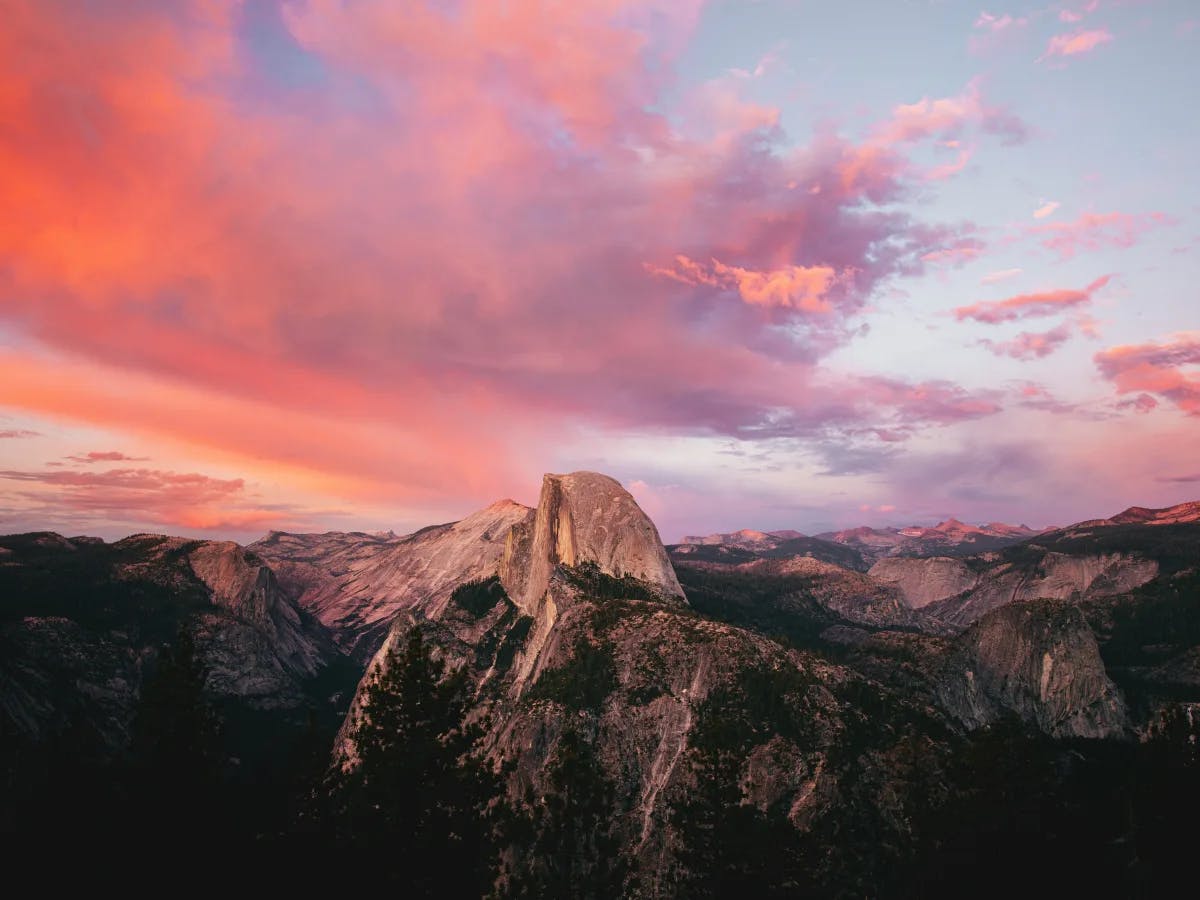 A vibrant sunset illuminates a mountainous landscape with dramatic rock formations and a colorful sky.