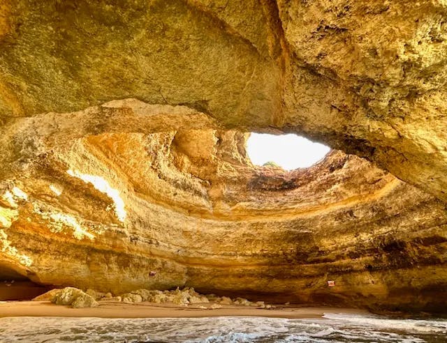 Water inside of Benagil Cave, a large rounded rock formation with a large opening in the top - Mindy Levin