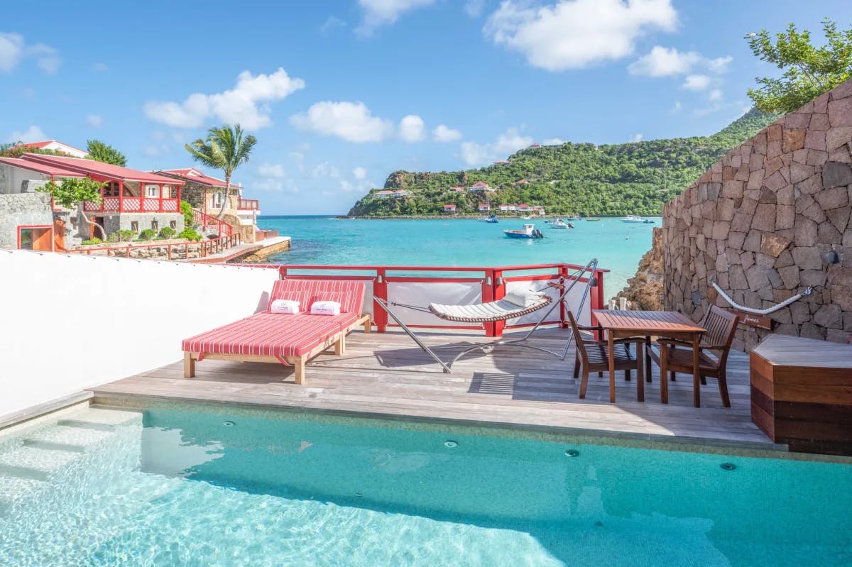 red lounge chairs on a wood pool deck with turquoise sea in the background