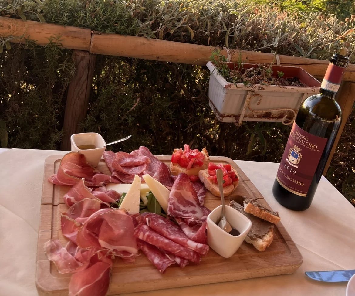 A charcuterie board with meat on an outdoor patio next to a bottle of wine. 