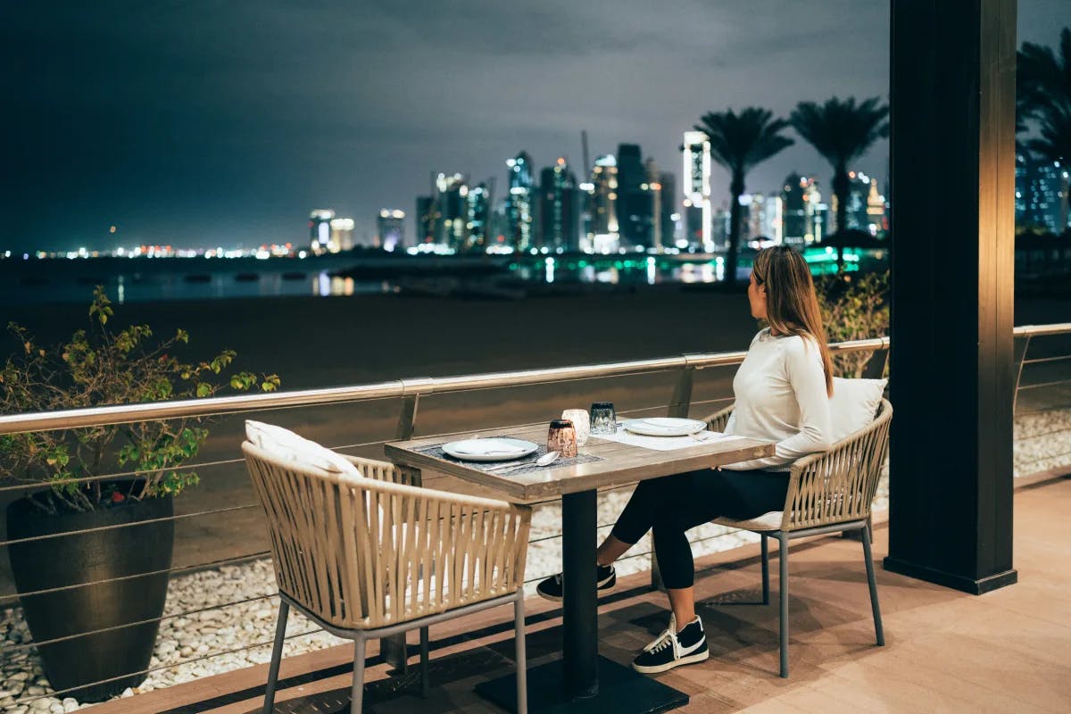 A waterfront dining experience with a view of the illuminated city skyline at night, inviting a moment of urban tranquility.