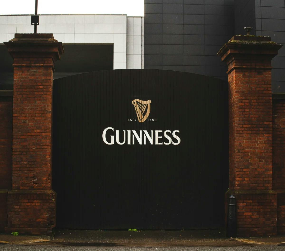 A black gate with the Guinness logo on it and brick columns on either side.