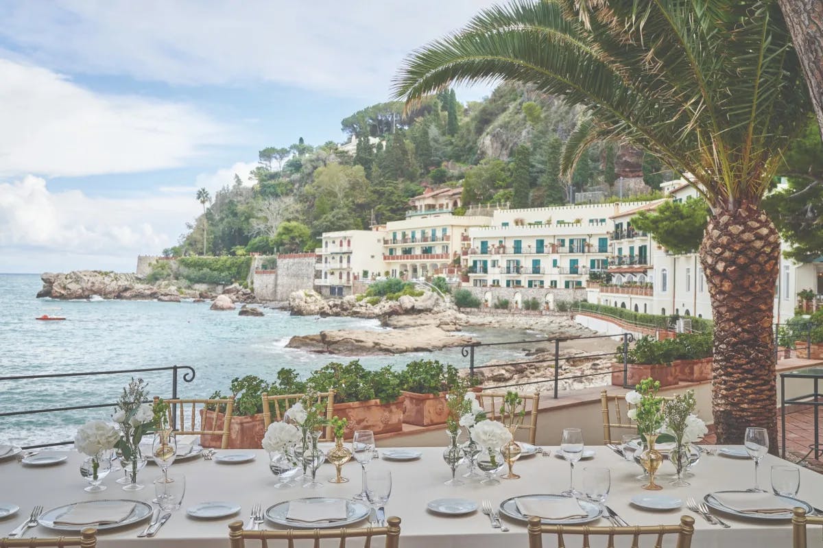 vantage point from outdoor dining table looking across blue sea to a white hotel with green shutters