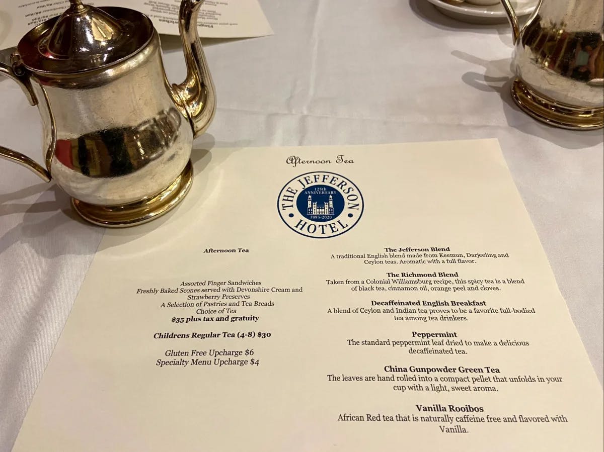 A tea menu from The Jefferson Hotel is displayed alongside a silver teapot and creamer set.