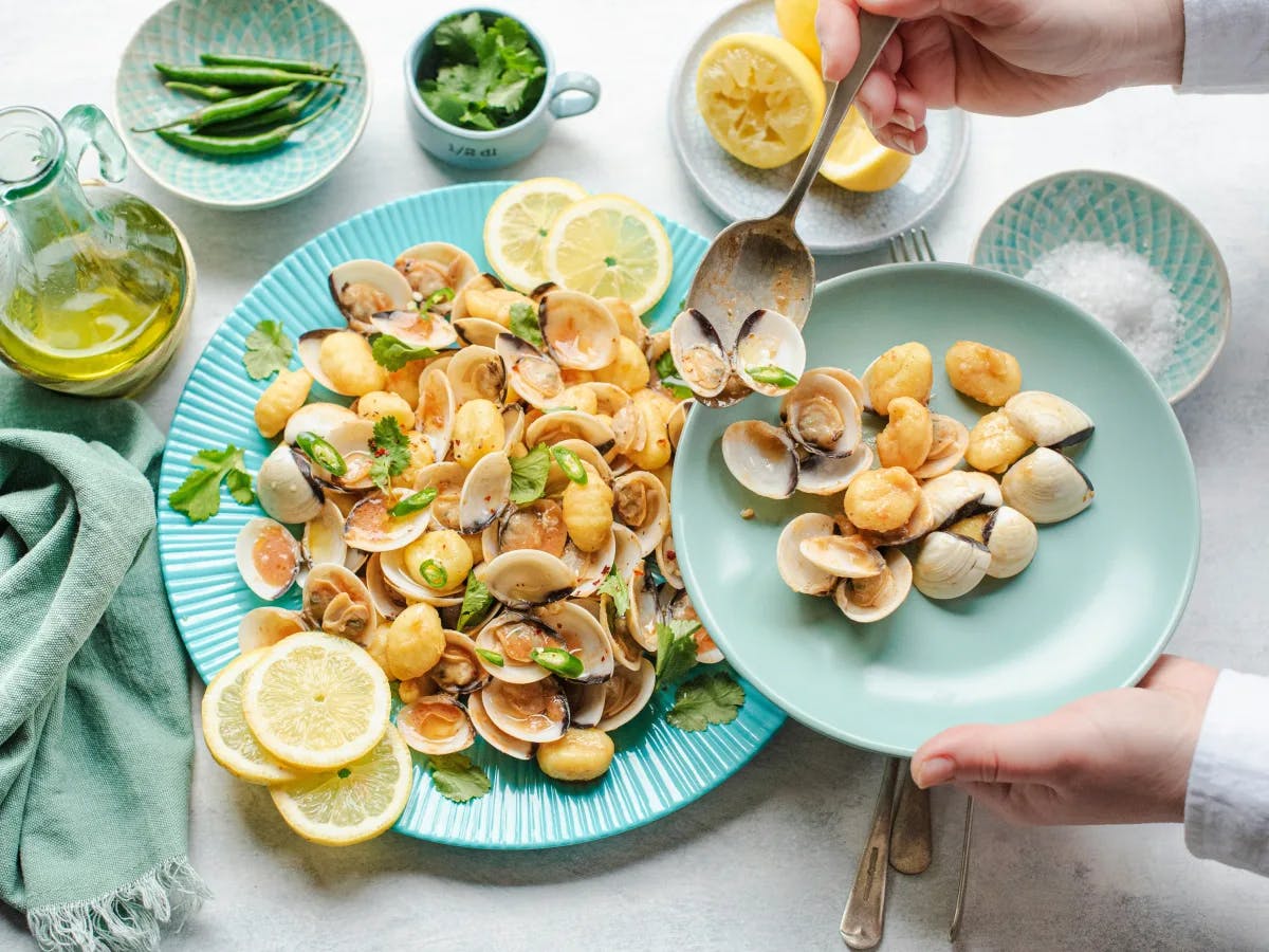 A platter of cooked clams served with lemon and chilies on a table on green and blue dishes