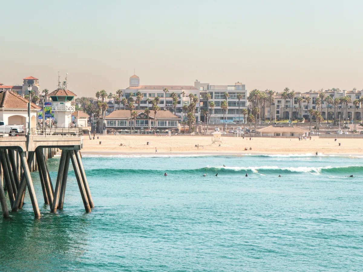 The image presents a serene coastal scene with a pier stretching into turquoise waters, bordered by a sandy beach and buildings under a clear sky.