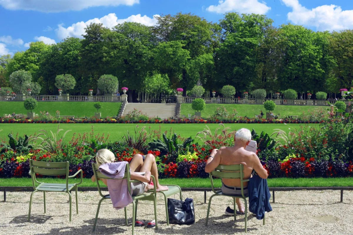 a shirtless man and a young woman sit on green chairs in a beautiful park on a sunny day