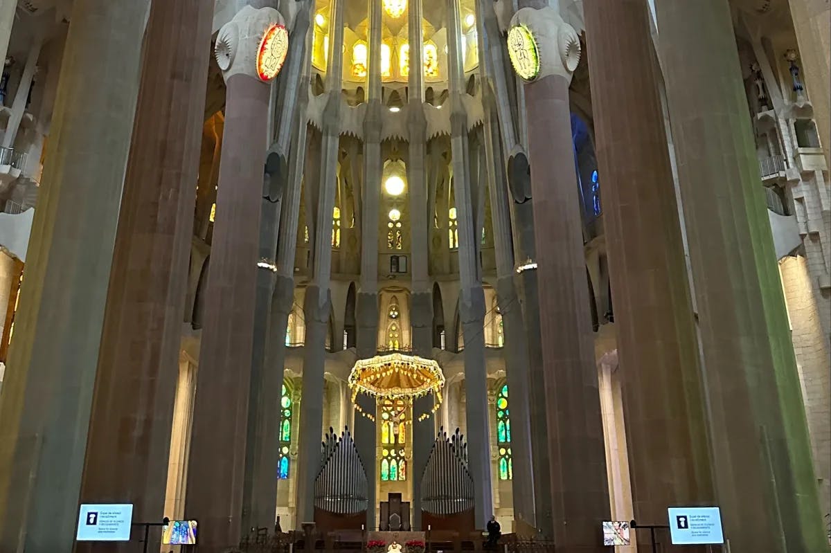 Inside La Sagrada Familia, showing a central illuminated altar with high ceiling