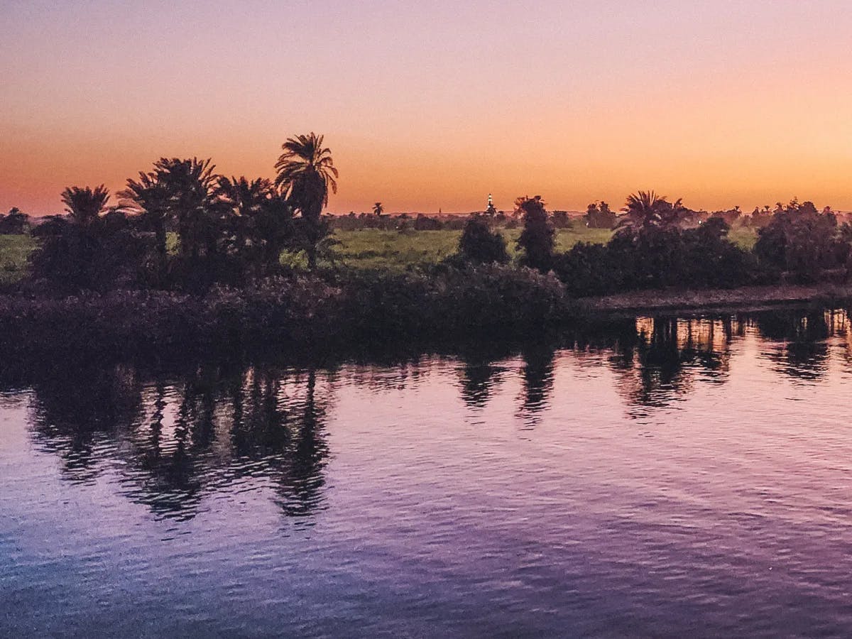 The Nile River at sunset with palm trees on the banks.